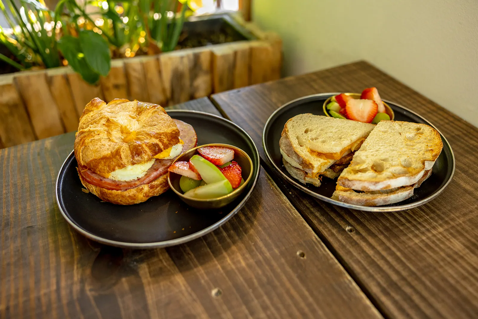 A breakfast spread of croissant sandwich and grilled cheese with fresh fruit