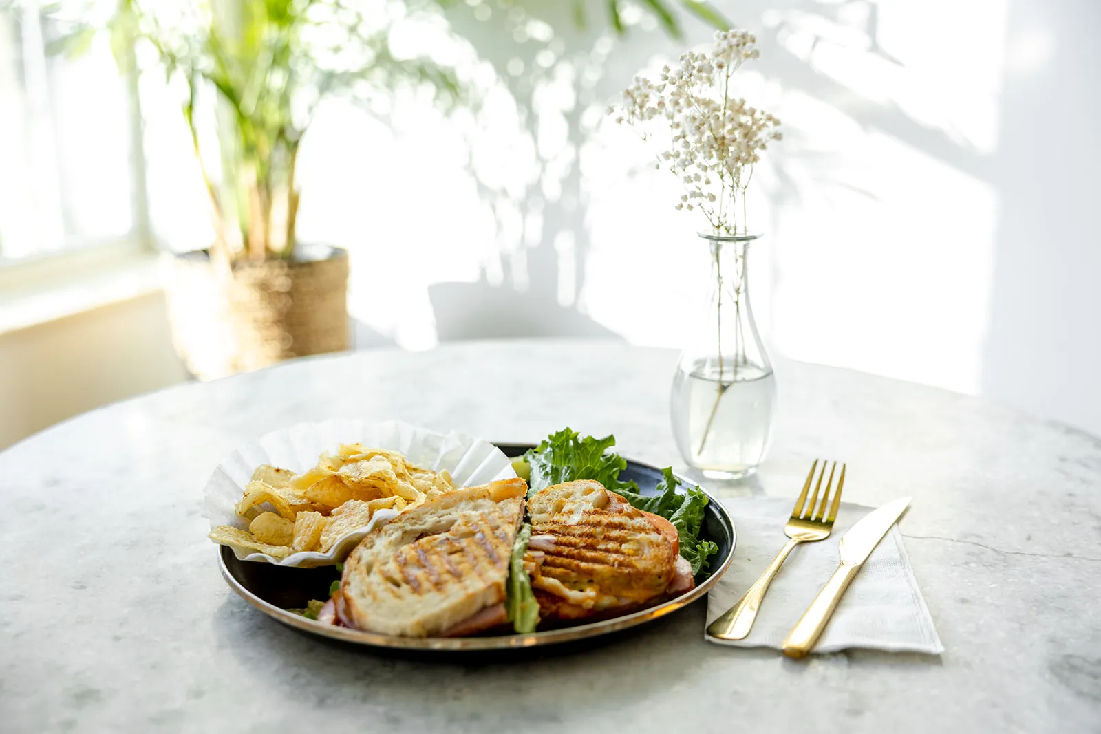 Grilled panini with kettle chips on marble, gold flatware and baby's breath
